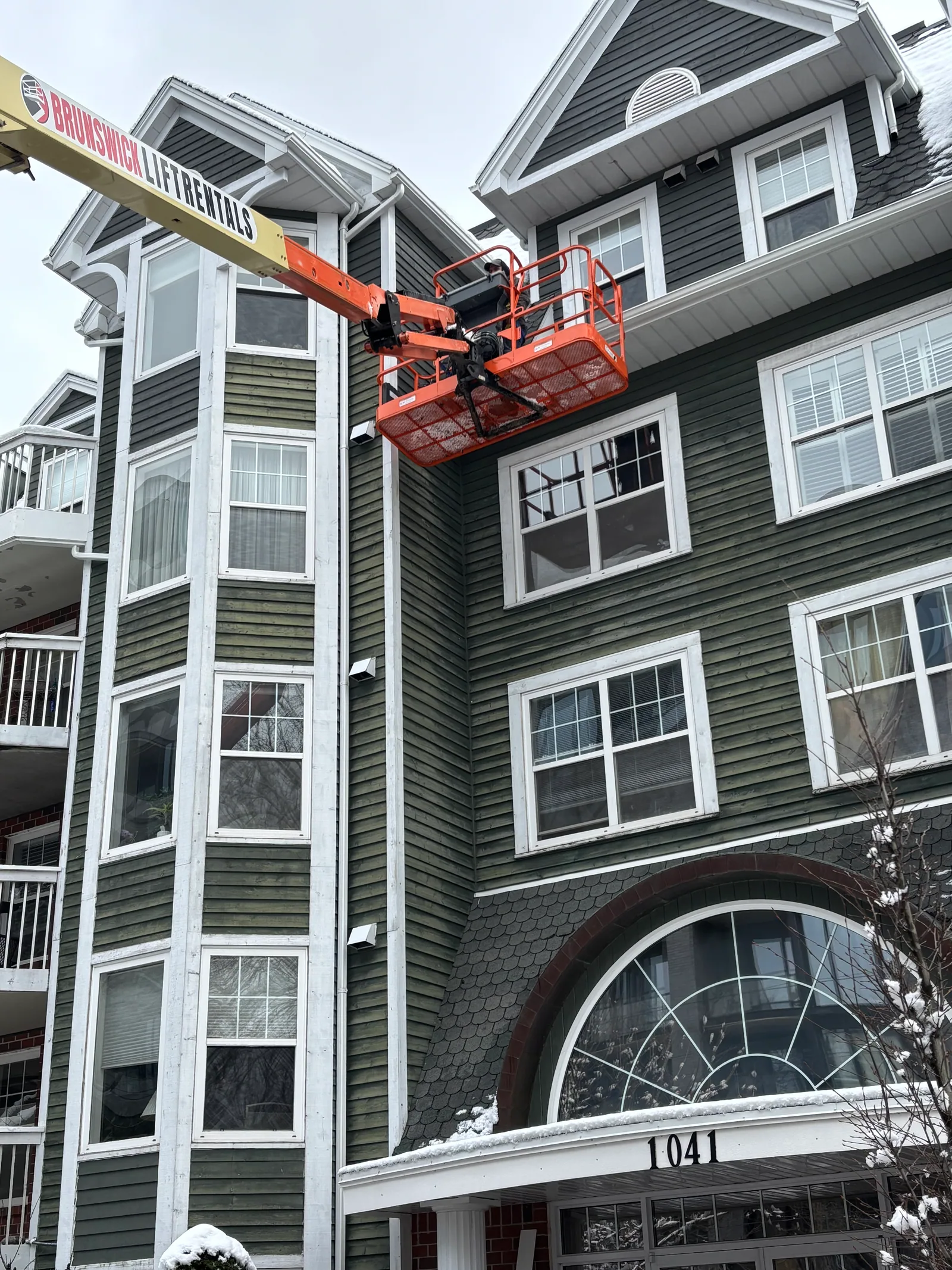Boom lift raised against a multi-unit building for high-access exterior repairs